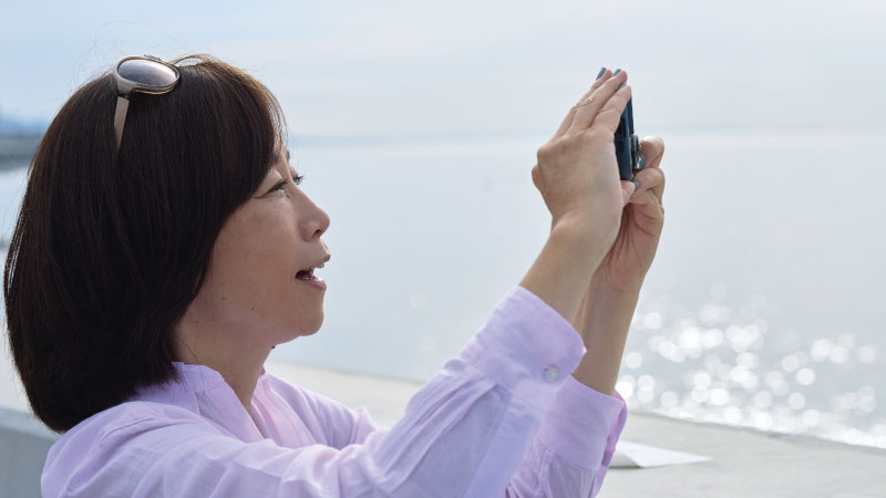 カートピア 海辺の景色をスマートフォンで撮影する飯田裕子さん | SUBARU