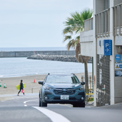 カートピア 茅ヶ崎の市街地を走るクロストレック。後ろには海が見えている | SUBARU