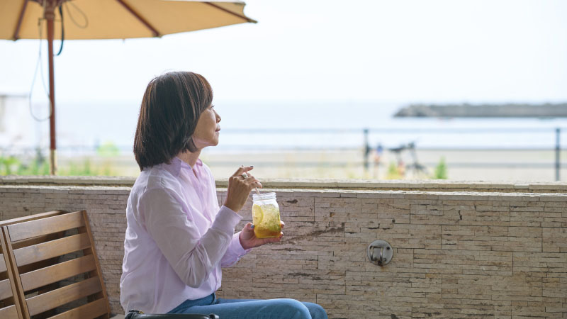 カートピア ビーチサイドにあるカフェのテラス席で、海を眺めながらレモネードを飲む飯田裕子さん | SUBARU