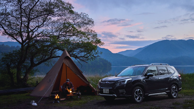 カートピア 夕景の中、フォレスターのそばでテントを張ってキャンプをしている様子 | SUBARU